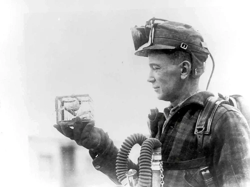 Historisches Schwarzweißfoto: Bergmann mit Grubenlampe hält einen kleinen Käfig mit Kanarienvogel